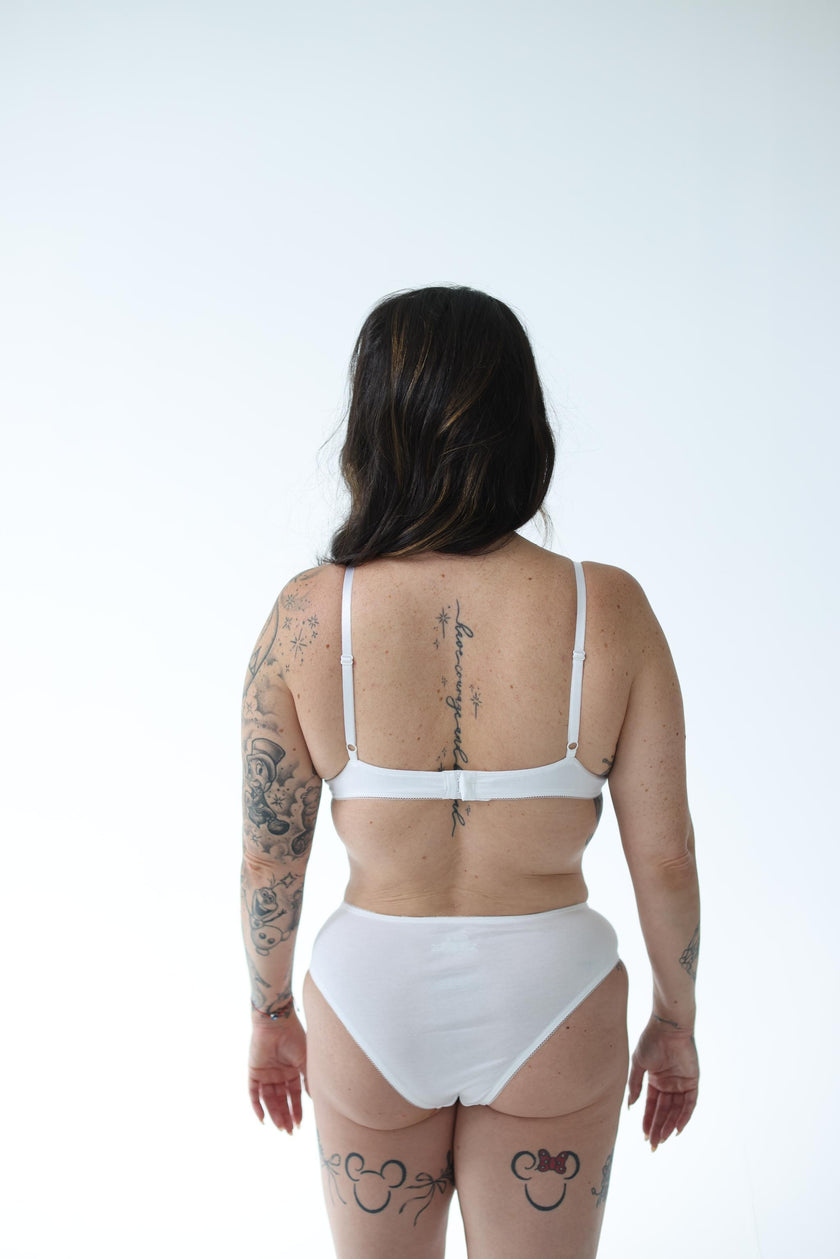 Person wearing white panties and bra on a plain background