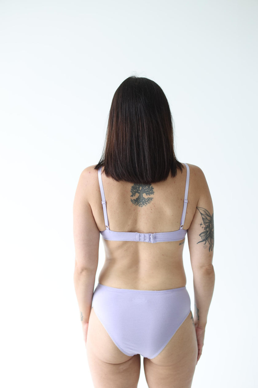 Person wearing a light purple bralette and pantie set on a white background