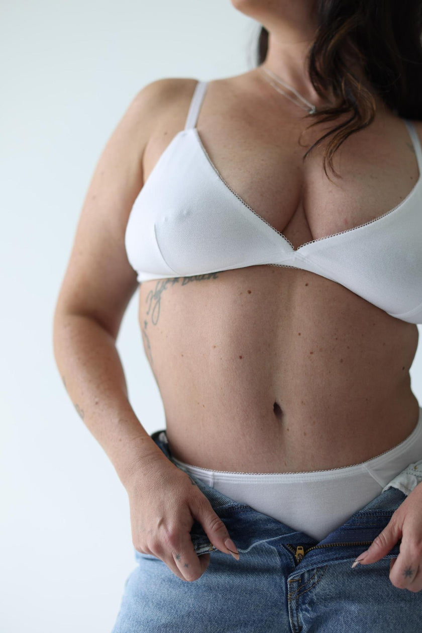 Person wearing a white bra and blue jeans against a plain background