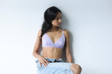 Woman wearing a light purple bralette against a plain background